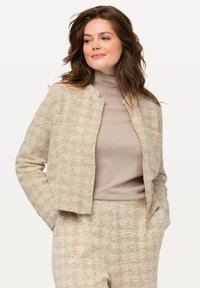 Beige textuur jasje met een subtiel patroon, cropped ontwerp en open voorkant. Draag het over een lichtbeige coltrui, met zichtbare zakdetails.