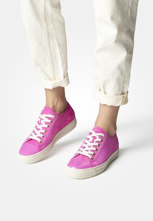 Sneaker rosa con upper liscia e punta lucida, dotate di lacci bianchi e occhielli dorati. Posizionate su jeans arrotolati di colore chiaro.