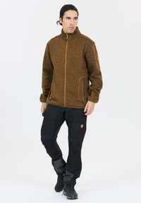 Giacca marrone tessurizzata con colletto alto, chiusura con zip e tasche laterali. Abbinata a pantaloni cargo neri con molteplici tasche e dettagli.