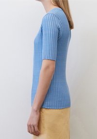 Světle modrý žebrovaný pletený top s krátkými rukávy a přiléhavým střihem, který zdůrazňuje texturovaný vzor a hladký povrch látky.