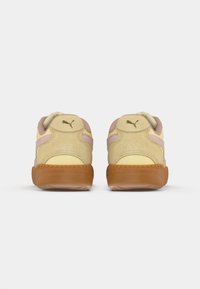 Puma sneakers with a light yellow suede upper, pink accents, round padded collar, and a brown rubber sole. Logo detail on the heel.