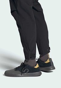 Czarno-szare sneakersy z nubukową i siateczkową cholewką, sznurówką i gumową podeszwą. Skarpety mają szare i żółte napisy. Regulowane mankiety spodni.