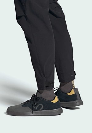 Czarno-szare sneakersy z nubukową i siateczkową cholewką, sznurówką i gumową podeszwą. Skarpety mają szare i żółte napisy. Regulowane mankiety spodni.