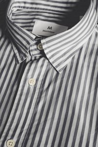 Sivo-bela majica z vzorcem črt in ovratnikom z gumbi, opremljena z belimi gumbi in oznako z napisom "Martineque" v kontrastni pisavi.