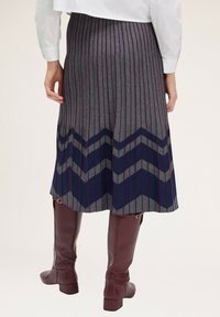 Grauer faltender Rock mit vertikalen Streifen und Chevron-Muster in Marineblau und Grau. Kombiniert mit bordeauxroten Leder-Stiefeln bis zur Wade.