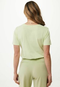 Světle zelený top s krátkým rukávem a volným střihem, nošený přes odpovídající světle zelené kalhoty, s kulatým výstřihem a měkkou texturou.