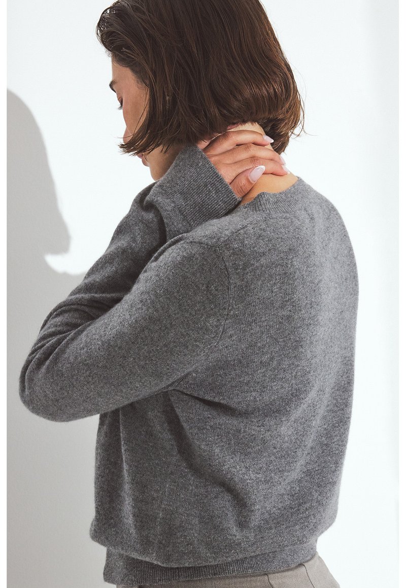 Suéter gris de punto con mangas largas, escote redondo y puños acanalados. Textura suave. El modelo se muestra de espaldas.
