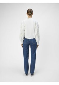 Blusa bianca con maniche volumetrice caratterizzata da dettagli in pizzo intricati, abbinata a jeans blu a vita alta e scarpe col tacco nere.