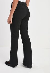 Zwarte, flared broeken met een gladde textuur en een middelhoge taille. Beschikt over zijzakken en een getailleerde pasvorm. Gecombineerd met zwarte flats.