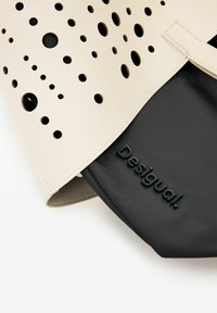 Fehér bőrtáska perforált körökkel, fekete szövet béléssel és a „Desigual” logóva beleüthették az elején.