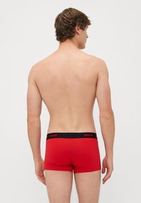 Boxer aderenti rossi con cintura elastica nera con il marchio "HUGO". Tessuto liscio e design aderente. Visualizzazione dal retro.