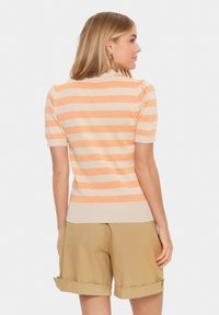 Gestreifter Strickpullover in Orange und Beige mit kurzen Puffärmeln und einem gerippten Saum. Getragen mit khakifarbenen Shorts mit umgeschlagenen Säumen.
