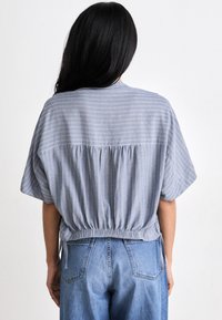 Lichtblauw topje met witte strepen, losse pasvorm, elastische gatherings bij de taille, korte mouwen, achteraanzicht, gecombineerd met hooggerande denim jeans.