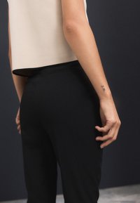 Fekete, testhez simuló nadrág sima textúrával, krémszínű, rövid fazonú toppal, tiszta, egyenes szegéllyel párosítva. A kar kitett bőrfelületén tetoválás látható.