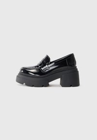 Svarta lackläderplattform loafers med en kraftig gummisula, med en moccasin-stil framtill och ett brett rem-accent över toppen.