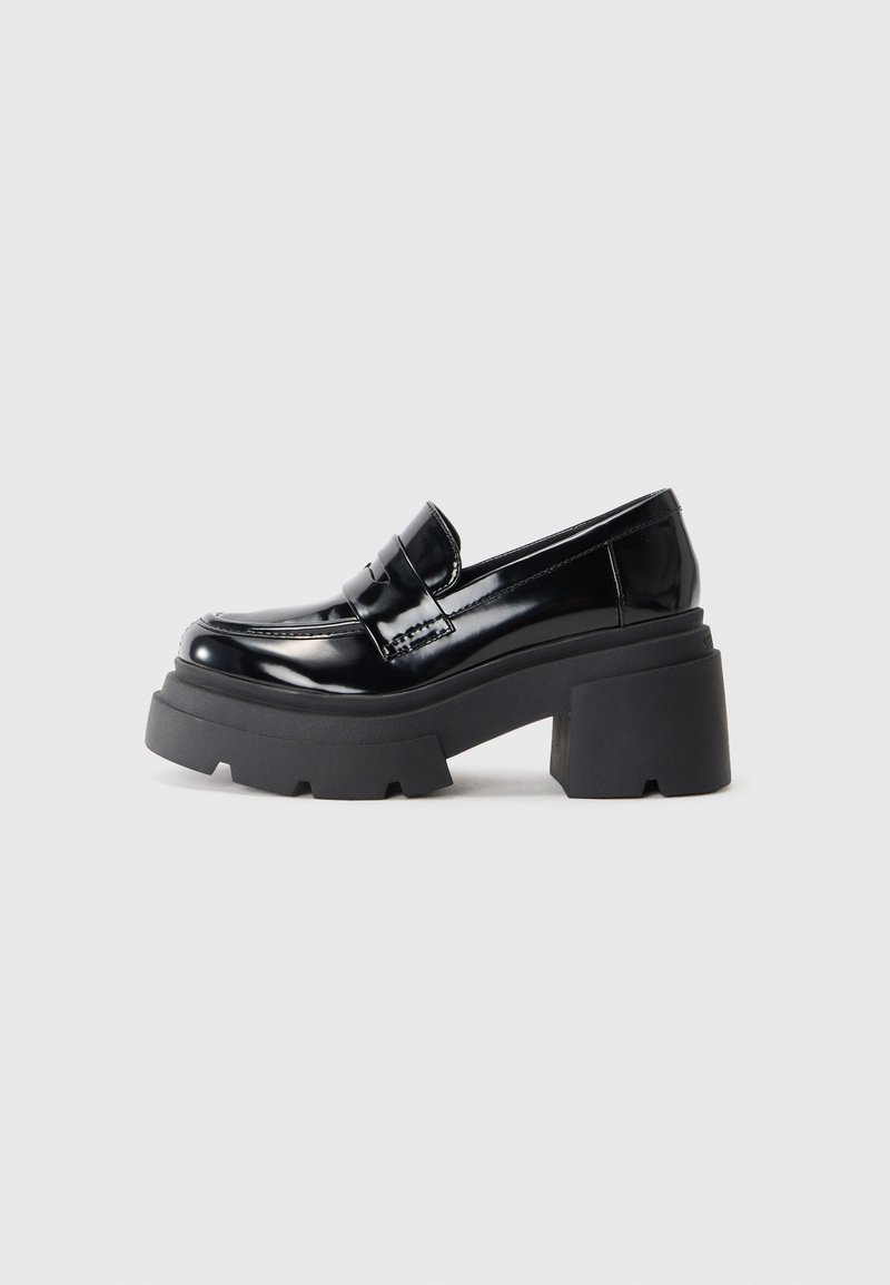 Svarta lackläderplattform loafers med en kraftig gummisula, med en moccasin-stil framtill och ett brett rem-accent över toppen.