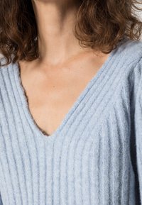 Jasnoniebieski dziany sweter z dekoltem w serek i pionową prążkowaną fakturą; miękki materiał i luźne dopasowanie na ramionach.