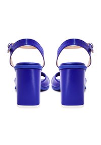 Blauwe leren sandalen met blokhak, enkelbandjes en zilveren gespen, gezien van achteren op een witte achtergrond.