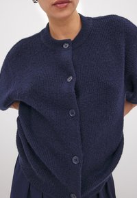Marineblauwe korte mouwen cardigan van gestructureerde brei-stof, met vijf knopen aan de voorkant en een ronde halslijn.