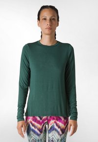 Maglia verde a maniche lunghe con scollatura rotonda, realizzata in un tessuto morbido e con una vestibilità comoda. Indossata con leggings colorati e con diversi motivi.