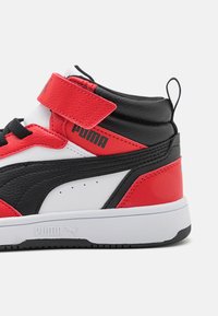 Baskets montantes Puma avec une tige synthétique rouge, noire et blanche, dotées d'une sangle Velcro, d'accents texturés et d'une semelle en caoutchouc blanche.