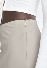 Beige skirt with a smooth, stretchy fabric, featuring a discreet side zipper. Paired with a white ribbed long-sleeve top.