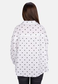 White shirt with black heart pattern, loose fit, long sleeves, and back yoke detail. Textured fabric with a casual design. Black pants visible.