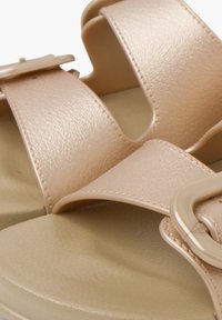 Tan sandals with two wide straps and a large buckle. Textured synthetic material. Soft, contoured footbed for comfort.