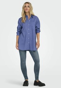 Blå rutiga oversized skjorta med knappframsida och ficka, tillsammans med skinny jeans och svarta loafers. Mjuk tyg och avslappnad passform.