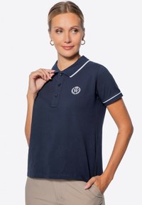 Polo shirt blu navy con bordo bianco, placca a tre bottoni e logo sul lato sinistro del petto. Realizzato in tessuto strutturato con vestibilità rilassata.