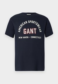 Tricou bleu marin cu text alb și roșu care spune "American Sportswear GANT New Haven - Connecticut" pe față.