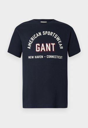 Tamno plava majica s bijelim i crvenim tekstom koji glasi "Američka Sportska Odjeća GANT New Haven - Connecticut" na prednjoj strani.