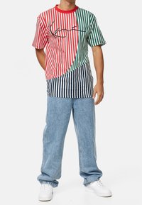 Camiseta de rayas multicolor con secciones rojas, verdes y azules y un cuello redondo. Combinada con jeans de denim claros y zapatillas blancas.