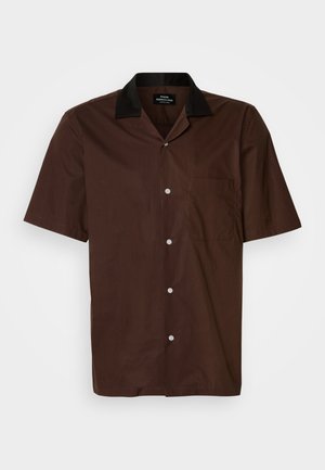 Kratka majica s kratkimi rokavi iz temno rjavega blaga z črnim ovratnikom. Ima eno žep na prsih in bele gumbe vzdolž sprednje strani.