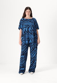 Zilā un melnā svītraina blūze un bikses, izgatavotas no mīksta auduma. Brīvs piegriezums ar platām piedurknēm un taisna piegriezuma siluets.