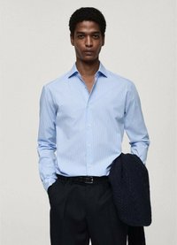 Cămașă albastră deschis, cu dungi verticale, mâneci lungi și croială lejeră. Purtați-o cu pantaloni închiși la culoare și țineți un sacou tricotat închis.