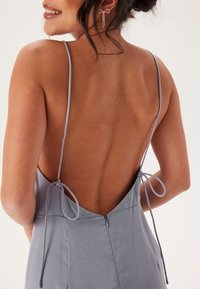 Bakvy av en ljusblå satinklänning med tunna justerbara band och en djup V-rygg, knuten med matchande tyg i nedre delen av ryggen.