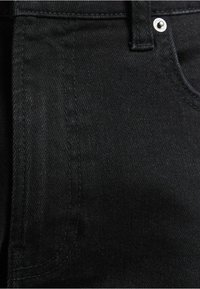 Primer plano de tela de mezclilla negra con costuras visibles y remache de metal cerca del borde del bolsillo.