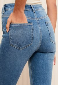 Sinine teksapüksid, millel on sobiv disain, keskmise kõrgusega vöökoht ja kaks tagataskut. Kanga tekstuur on sile ning nähtavad õmblused lisavad detaili.