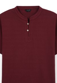 Polo henley corto color bordeaux realizzato in tessuto testurizzato, con un'apertura a tre bottoni e colletto arrotondato. Etichetta del marchio: Calliope.