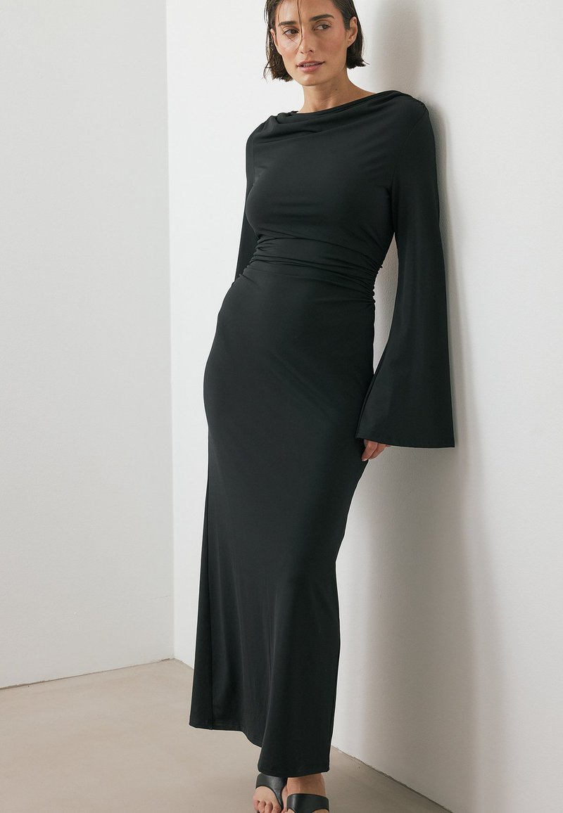 Svart långärmad klänning med figursydd överdel, draperad halsringning och utsvängda ärmar, tillverkad av ett glatt, elastiskt tyg. Enkel och elegant design.