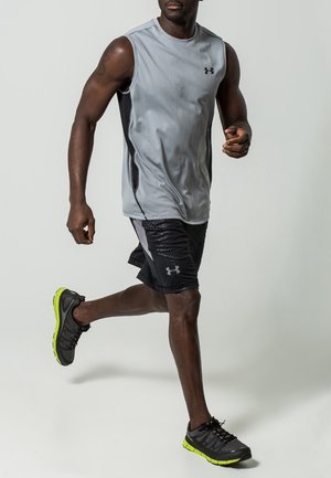 Grå ärmlös sporttopp med svarta detaljer, kombinerad med svarta shorts med texturerad panel och svarta löparskor med neon-gula sulor.