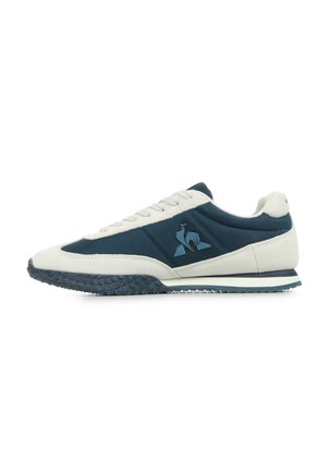 Scarpa da ginnastica blu e crema con suola in gomma testurizzata, parte superiore in suede e sintetico, punta tonda e dettagli con logo sul lato.