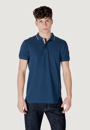 Polo blu scuro con colletto a bottoni, caratterizzato da leggere righe sul colletto, maniche corte e un design aderente. Indossato con jeans scuri.