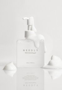 Vit fyrkantig flaska med pump, fylld med en mjölkaktig rengöringsgel. Bubblor och skum täcker delvis flaskan och ytan.