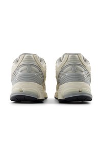 Pair of beige and gray New Balance running shoes seen from the back on a white background.