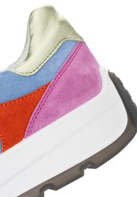Zbliżenie na piętę trampka z kolorowymi panelami zamszowymi w różowym, niebieskim i czerwonym kolorze, metalicznym złotym kołnierzem, białą podeszwą i czarnym bieżnikiem.