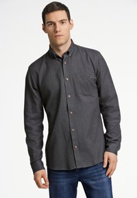 Camicia button-up grigio scuro con colletto, taschino sul petto e bottoni marroni. Realizzata in tessuto testurizzato, abbinata a jeans in denim blu.