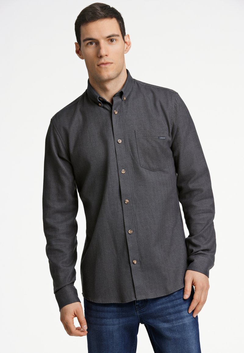 Camicia button-up grigio scuro con colletto, taschino sul petto e bottoni marroni. Realizzata in tessuto testurizzato, abbinata a jeans in denim blu.