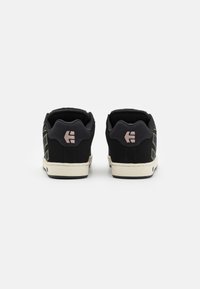 Black suede sneakers with textured detailing, contrasting green patterns, and a cream rubber sole. Features reinforced heel and logo accents.